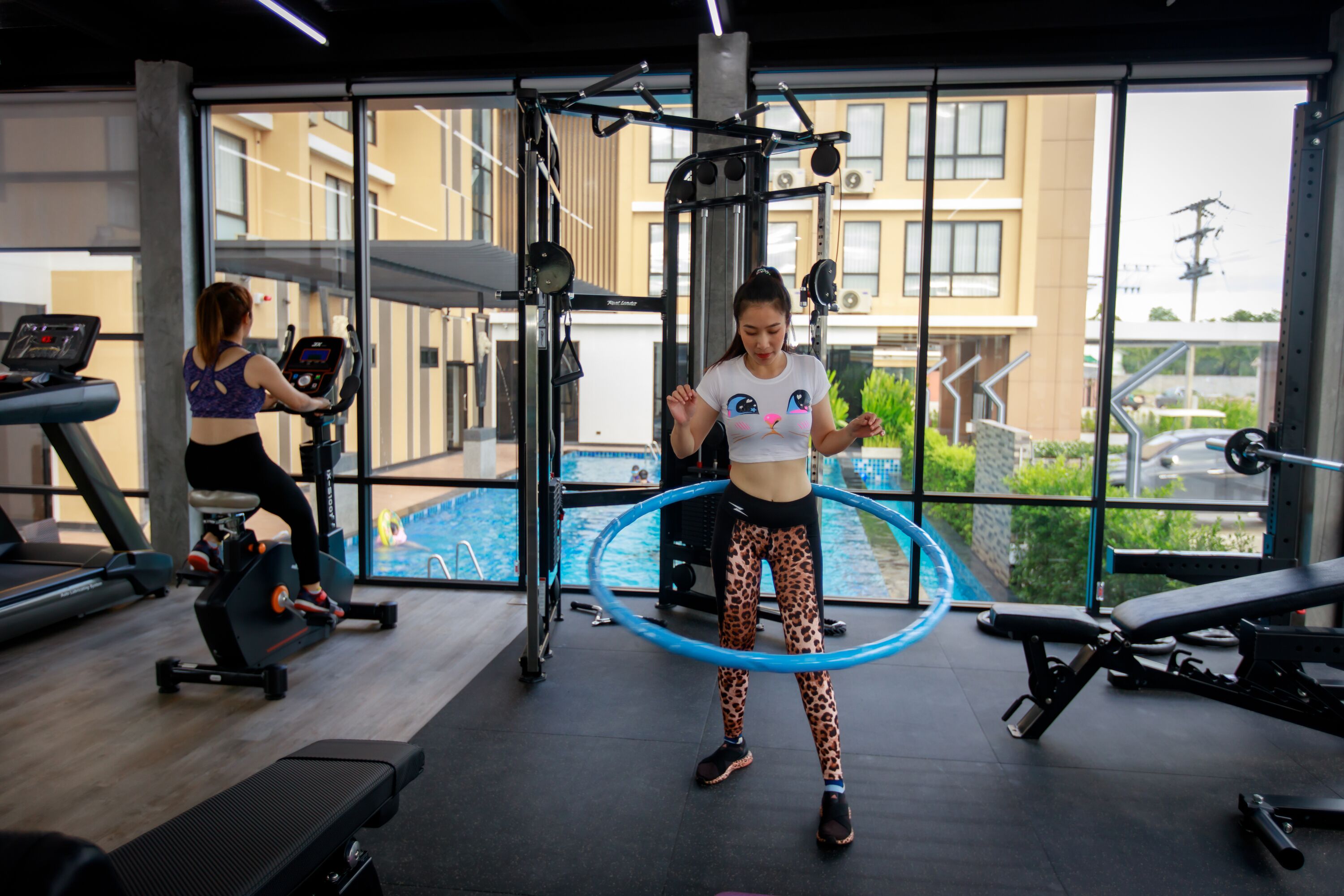 A gym with exercise equipment, large windows, and a view of a building outside.