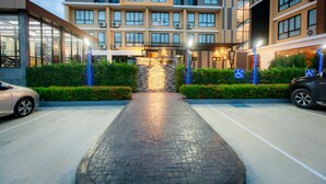 A hotel entrance with a paved pathway leading to the entrance, a parking area on either side, and a multi-story building with balconies. - Siri Hotel Lumphun (Lamphun)