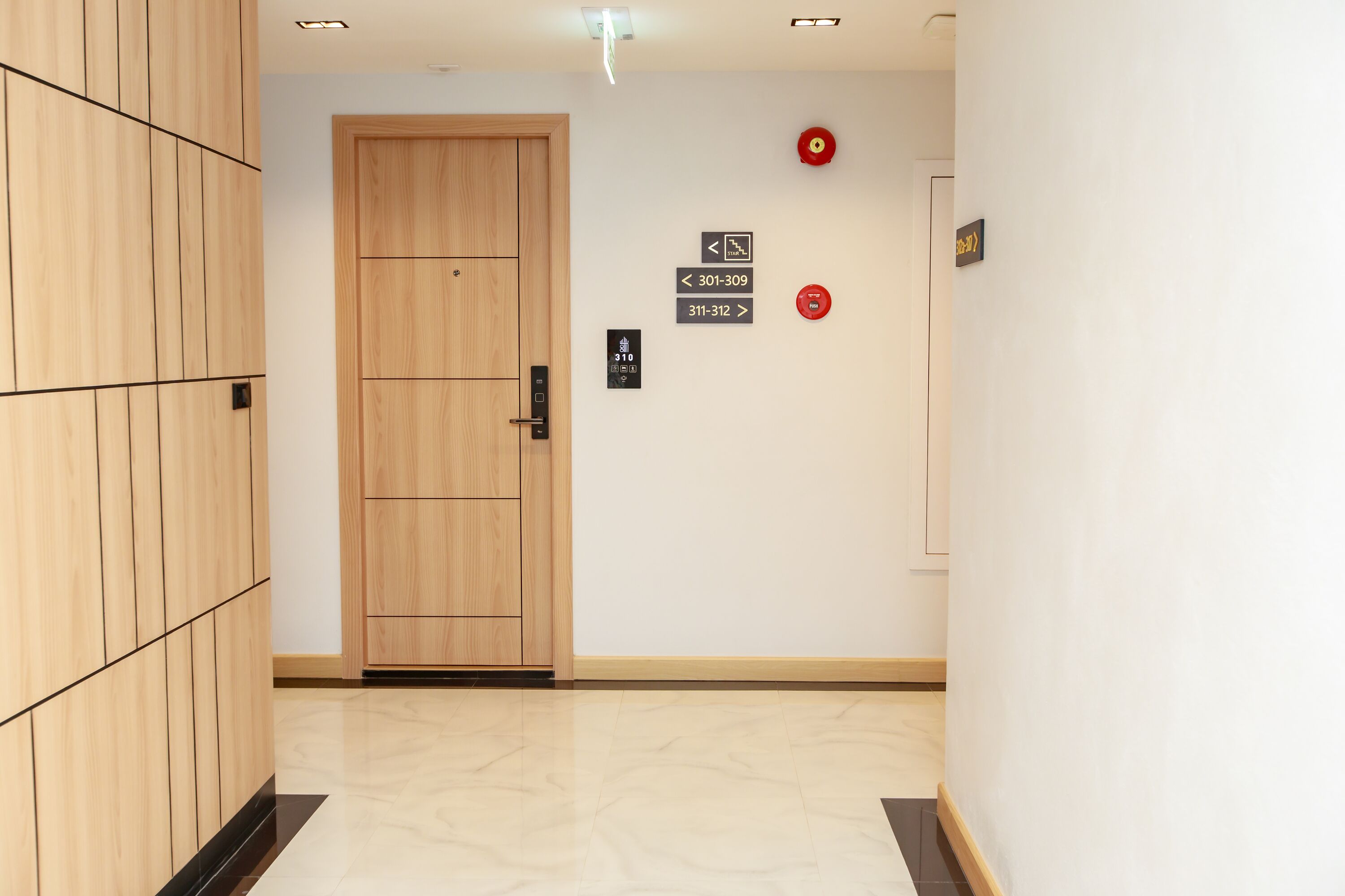 A hallway with a wooden door, emergency exit signs, and a fire alarm.