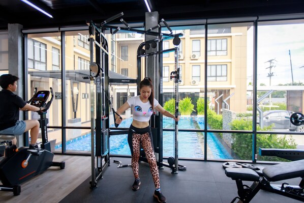 Un gimnasio con equipo de ejercicio, una caminadora y vistas a una piscina y edificios.