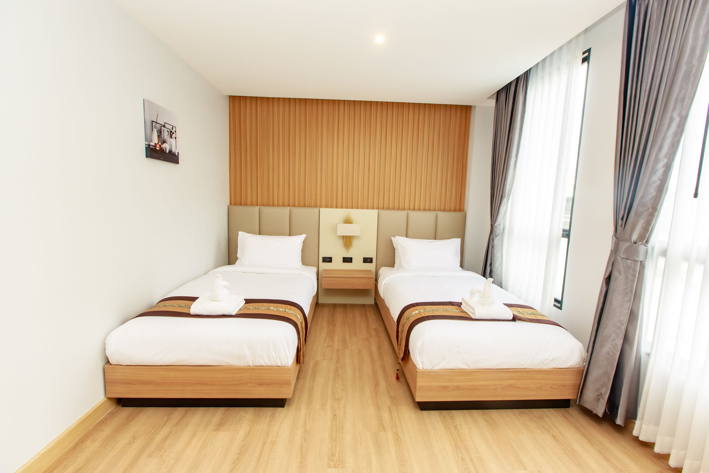 Habitación de hotel con dos camas, cabecera de madera, mesita de noche y ventana con cortinas.