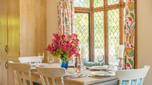 A dining table set for four with white chairs, a vase of pink flowers, and candles. - The Gate House - sleeps 4 guests  in 2 bedrooms (Folkestone)