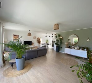 Un vaste espace de vie comprenant un canapé gris, une table à manger et une cuisine en arrière-plan.