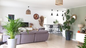 A modern living room with a grey sofa, a dining area with a white table, and a kitchen in the background. - Modern villa with all comforts (Saint-Génies-des-Mourgues)