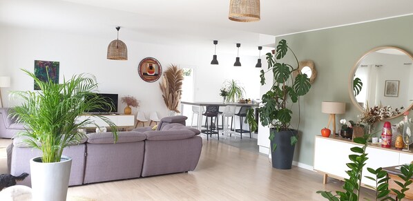 Un salon moderne avec un canapé gris, un coin repas avec une table blanche et une cuisine en arrière-plan.