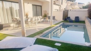 A modern outdoor pool area with a small pool, green artificial grass, and white cushions. - Modern villa with all comforts (Saint-Génies-des-Mourgues)
