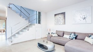 Uma sala de estar moderna com escada, um sofá cinzento com almofadas estampadas e arte floral abstrata nas paredes.