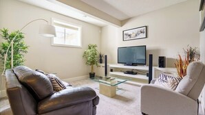 A modern living room with a leather sofa, a glass coffee table, a flat-screen TV, and a minimalist decor. - The Premier Suite | 321Mbps WiFi | Perfect Stays (Airdrie)