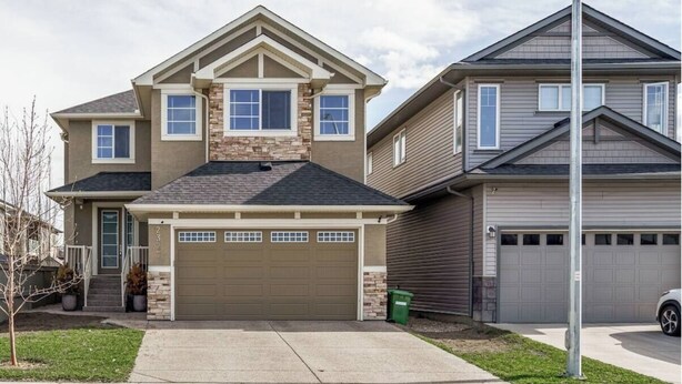 A two-story house with a garage, a stone facade, and a well-maintained lawn. - The Premier Suite | 321Mbps WiFi | Perfect Stays (Airdrie)