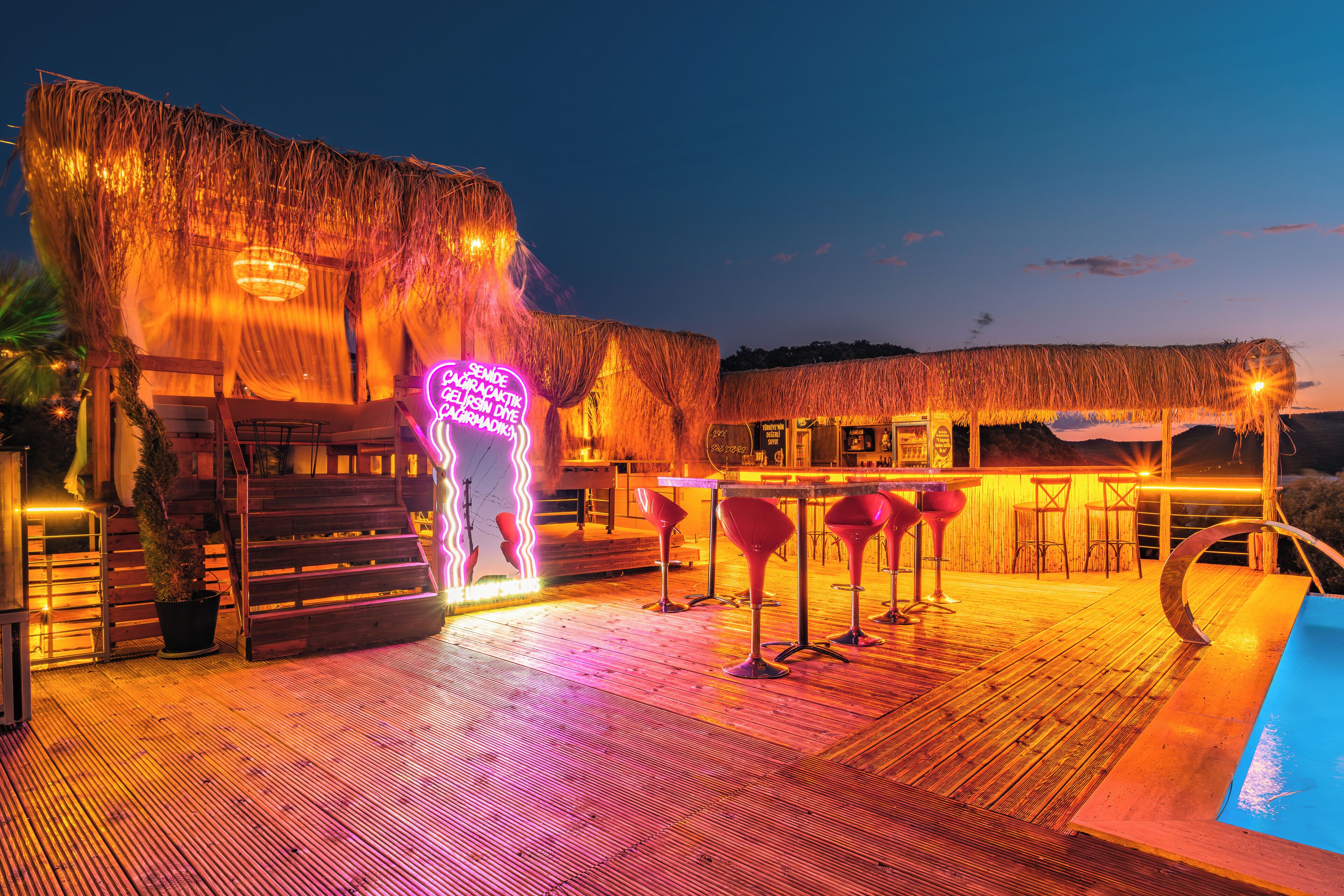 A wooden deck with a pool, bar area, and thatched-roof structures.