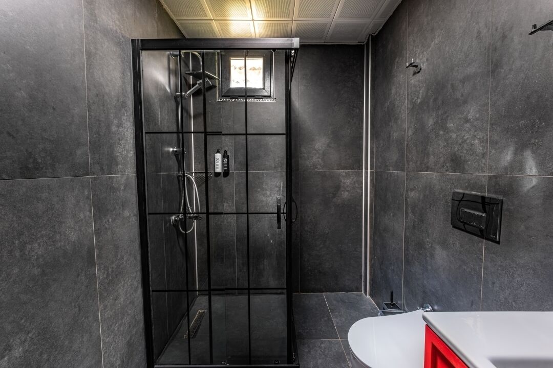A modern bathroom with a glass-enclosed shower, a white sink, and dark tiled walls.
