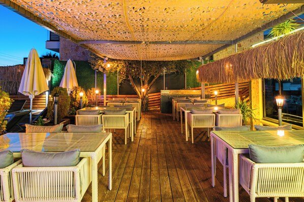 An outdoor patio with wicker furniture, umbrellas, and a thatched roof. - The Luxury Shelters (Kas)