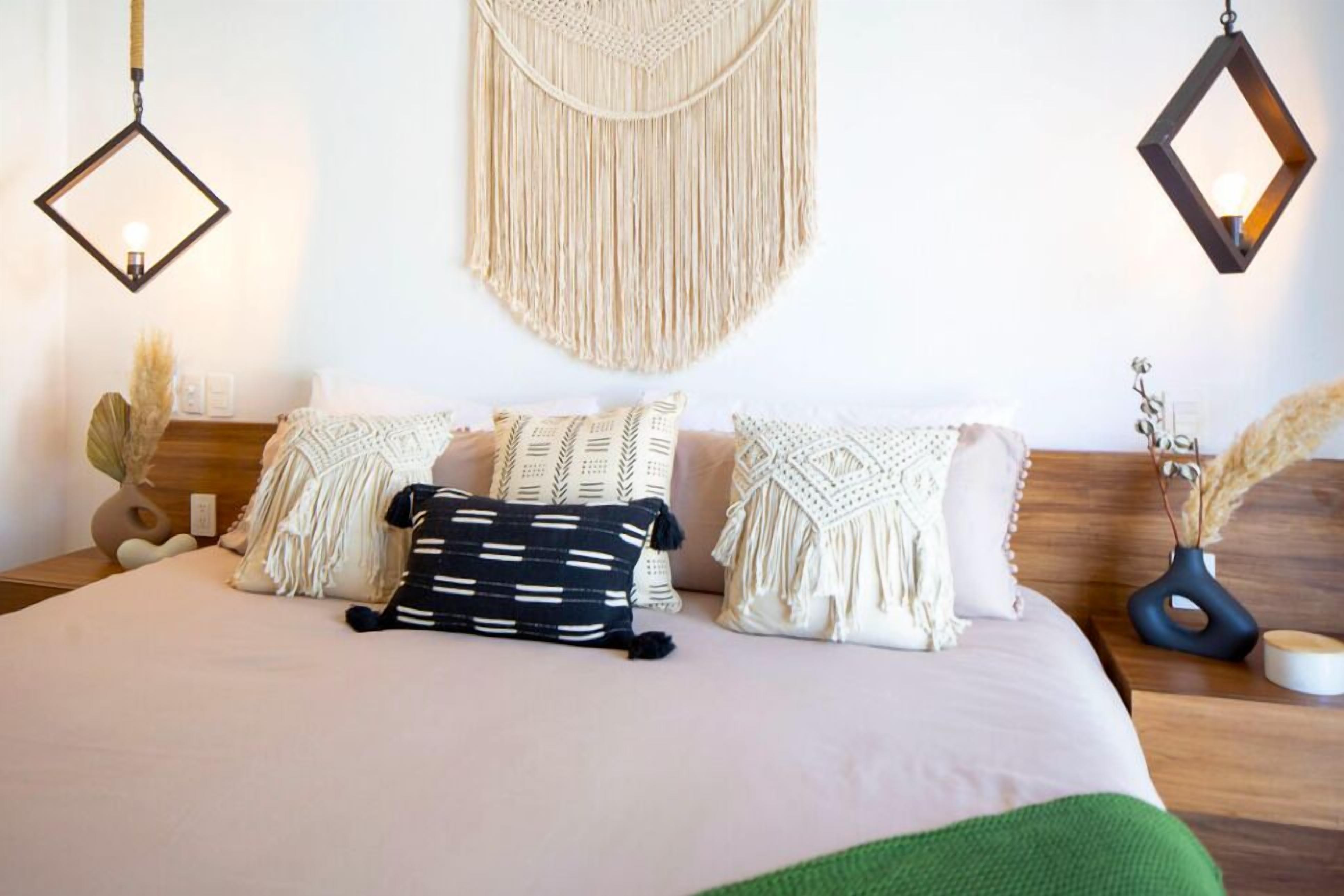 A neatly arranged bedroom with a bed, macramé wall hanging, and two wall-mounted lights.