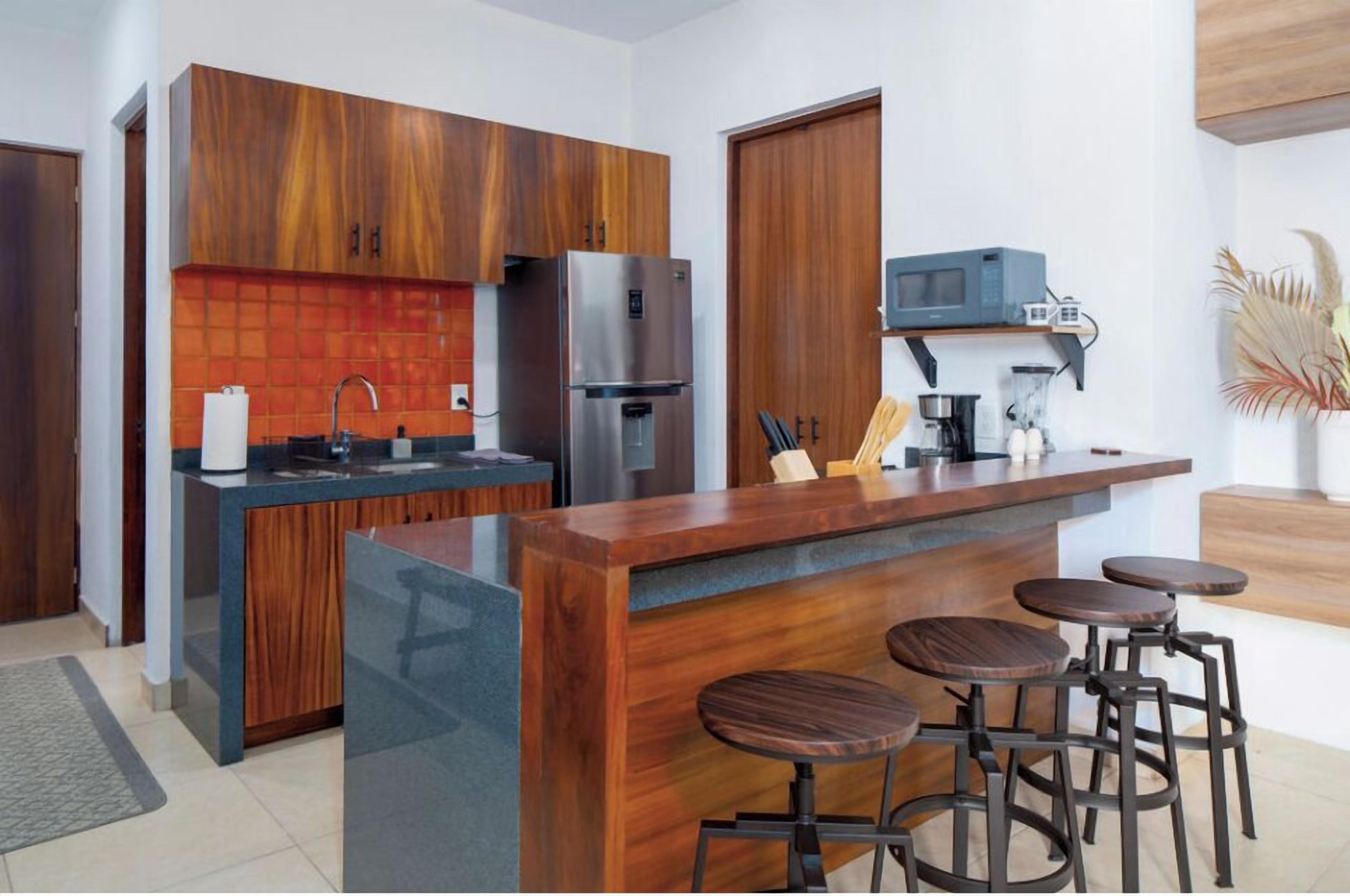 Une cuisine moderne avec des meubles en bois, un îlot central doté de tabourets, un réfrigérateur, un four à micro-ondes et une machine à café.