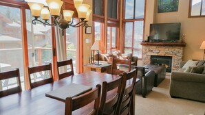 Un comedor con mesa y sillas de madera, chimenea, televisor y sofá.