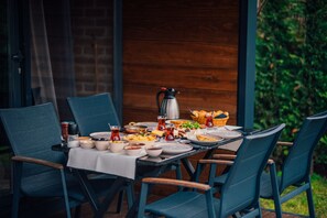 Un área de comedor al aire libre con una mesa lista para una comida, rodeada de sillas y una cafetera sobre la mesa.