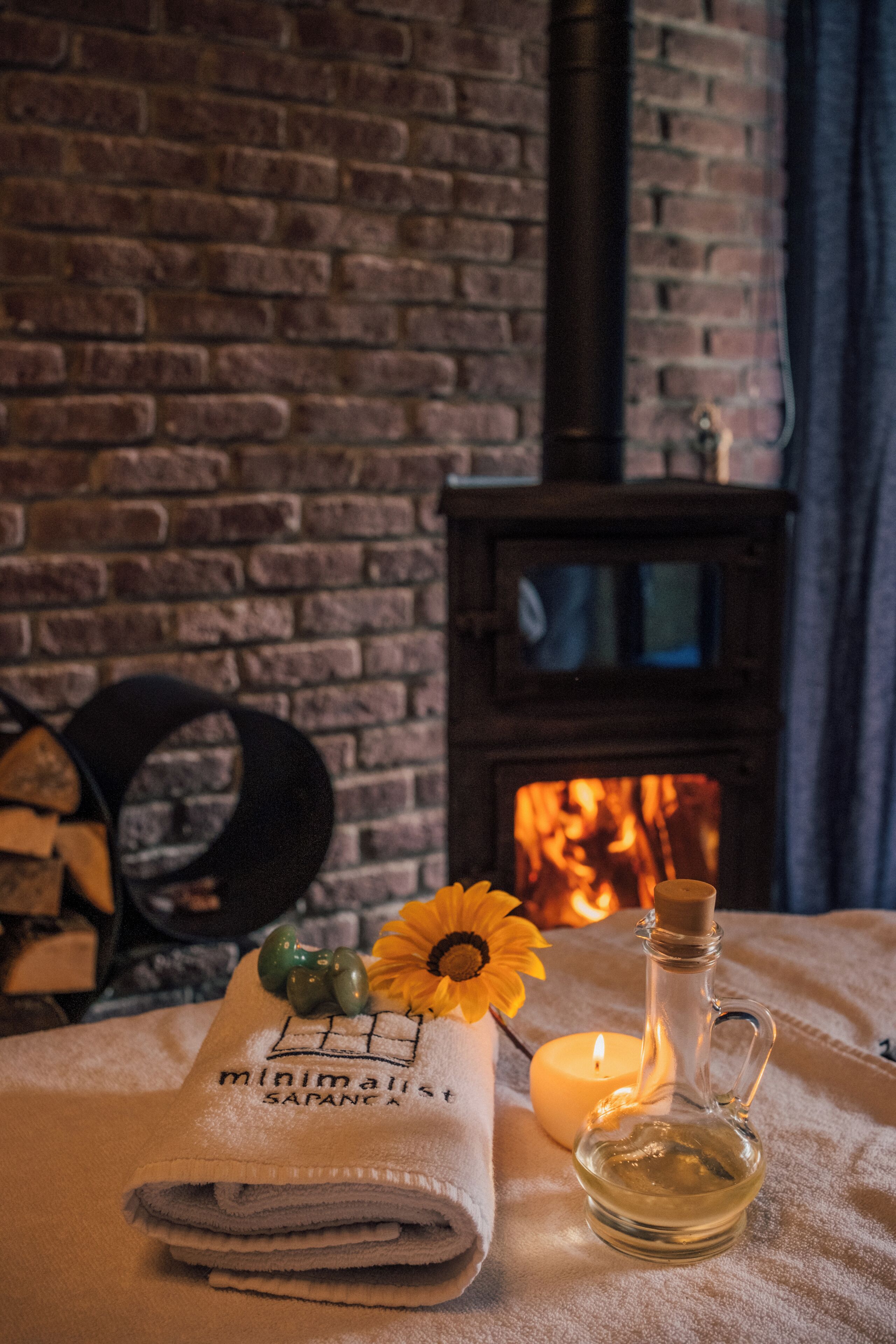 A cozy room with a brick fireplace, a folded towel, a candle, and a bottle of oil.