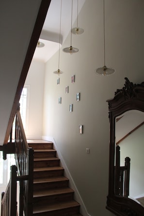 A wooden staircase with a handrail, a large mirror on the right, and pendant lights hanging from the ceiling.