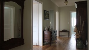 Een ruime hal met houten vloeren, een houten dressoir, een bankje en een vaas met pluimgras.