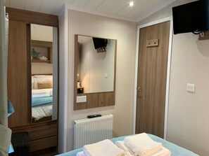 A hotel room with a bed, a mirror, a wardrobe, a radiator, and a TV mounted on the wall. - Gorgeous Coastal Holiday Home (Poole)