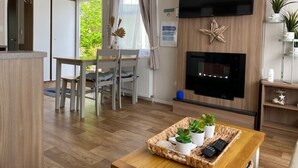 Uma sala de estar moderna com televisão de tela plana, piso de madeira, área de jantar com cadeiras e lareira.