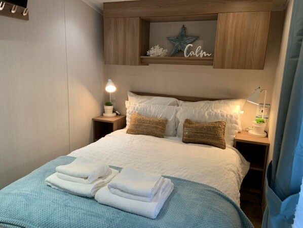 A neatly made bed with white linens and two pillows, a bedside table with a lamp, and a shelf above the bed with a star decoration and a 'Calm' sign. - Gorgeous Coastal Holiday Home (Poole)