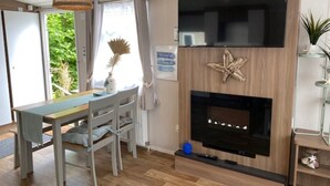 Uma sala de estar moderna com piso de madeira, uma mesa de jantar com cadeiras, uma TV fixada em uma parede de madeira e uma lareira.