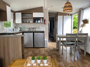 A modern kitchen with wooden cabinets, a built-in microwave, and a small refrigerator. There is a dining area with a table and chairs, and a basket of plants on the floor.
