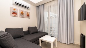 A modern living room with a grey sectional sofa, a small white table, and a flat-screen TV. - Kas Evderhan (Kas)