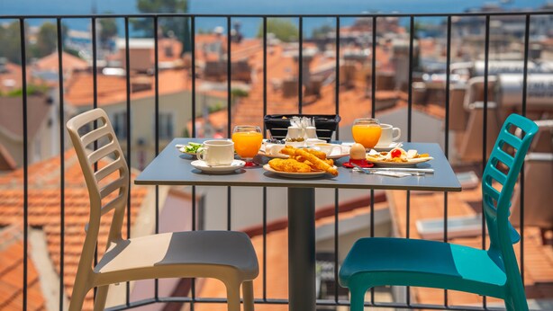 A balcony with a table set for breakfast, overlooking a cityscape. - Kas Evderhan (Kas)