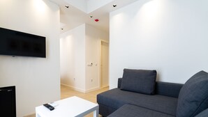 A modern living room with a grey sofa, a white coffee table, and a flat-screen TV mounted on the wall. - Kas Evderhan (Kas)