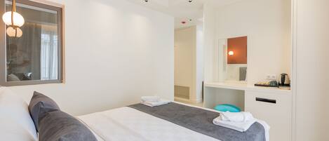 A modern hotel room with a neatly made bed, a small seating area, and a bathroom with a mirror and sink.
