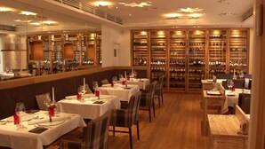 A restaurant with multiple tables set for dining, a wine cellar in the background, and a modern ceiling design. - Alpin Lifestyle Hotel Löwen & Strauss (Oberstdorf)