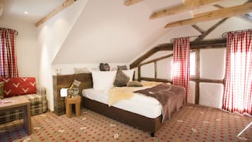 A bedroom with a sloped ceiling, a bed with a brown headboard, a red and white checkered curtain, and a patterned carpet.