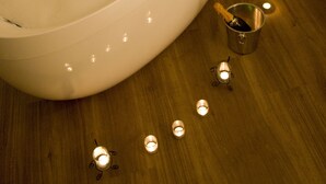 A bathtub filled with water and rose petals, surrounded by candles on a wooden floor. - Alpin Lifestyle Hotel Löwen & Strauss (Oberstdorf)