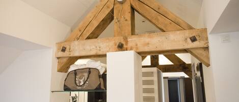 A room with exposed wooden beams, a glass shelf with a handbag, and a door leading to another room.