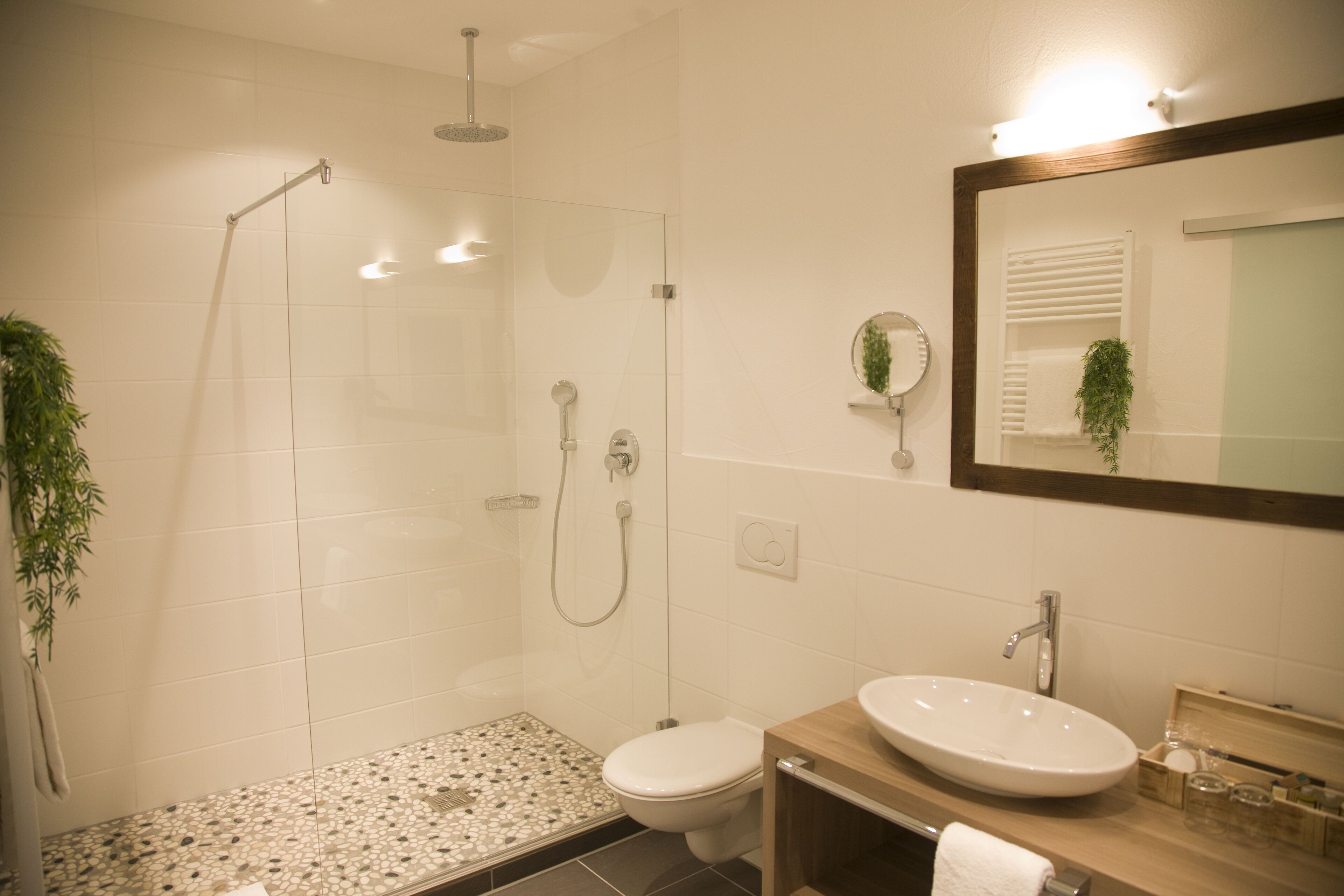 Un baño moderno con ducha envuelta en vidrio, inodoro y lavamanos con espejo.