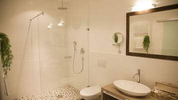 Un baño moderno con ducha envuelta en vidrio, inodoro y lavamanos con espejo.