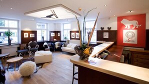 A modern hotel lobby with a reception desk, seating area, and large windows. - Alpin Lifestyle Hotel Löwen & Strauss (Oberstdorf)