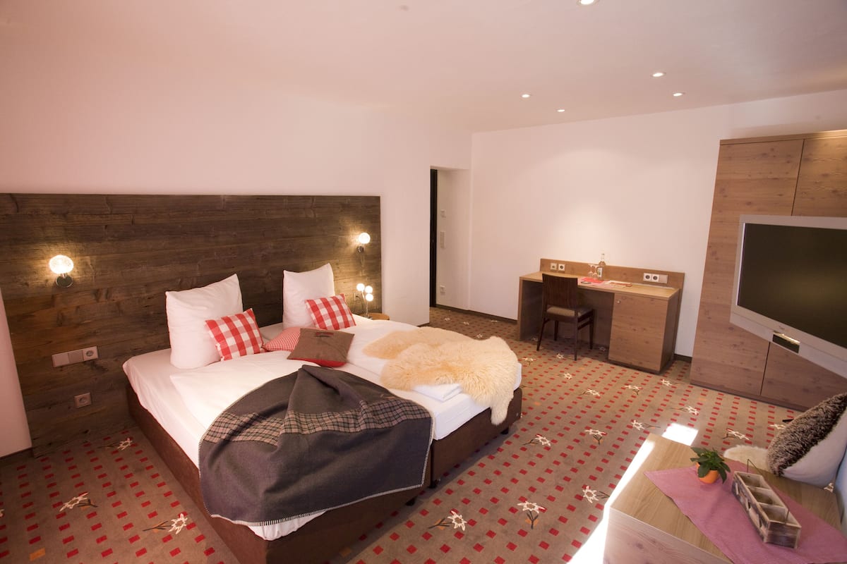 Habitación de hotel con cabecera de madera, cama con ropa blanca, escritorio, una silla y un televisor de pantalla plana.