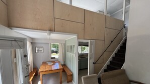 A spacious room with a wooden dining table, a sofa, and a staircase leading to an upper level.