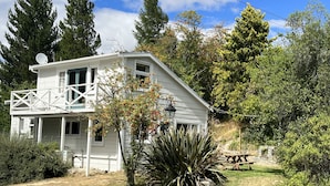 A white two-story house with a balcony, surrounded by trees and a grassy yard.