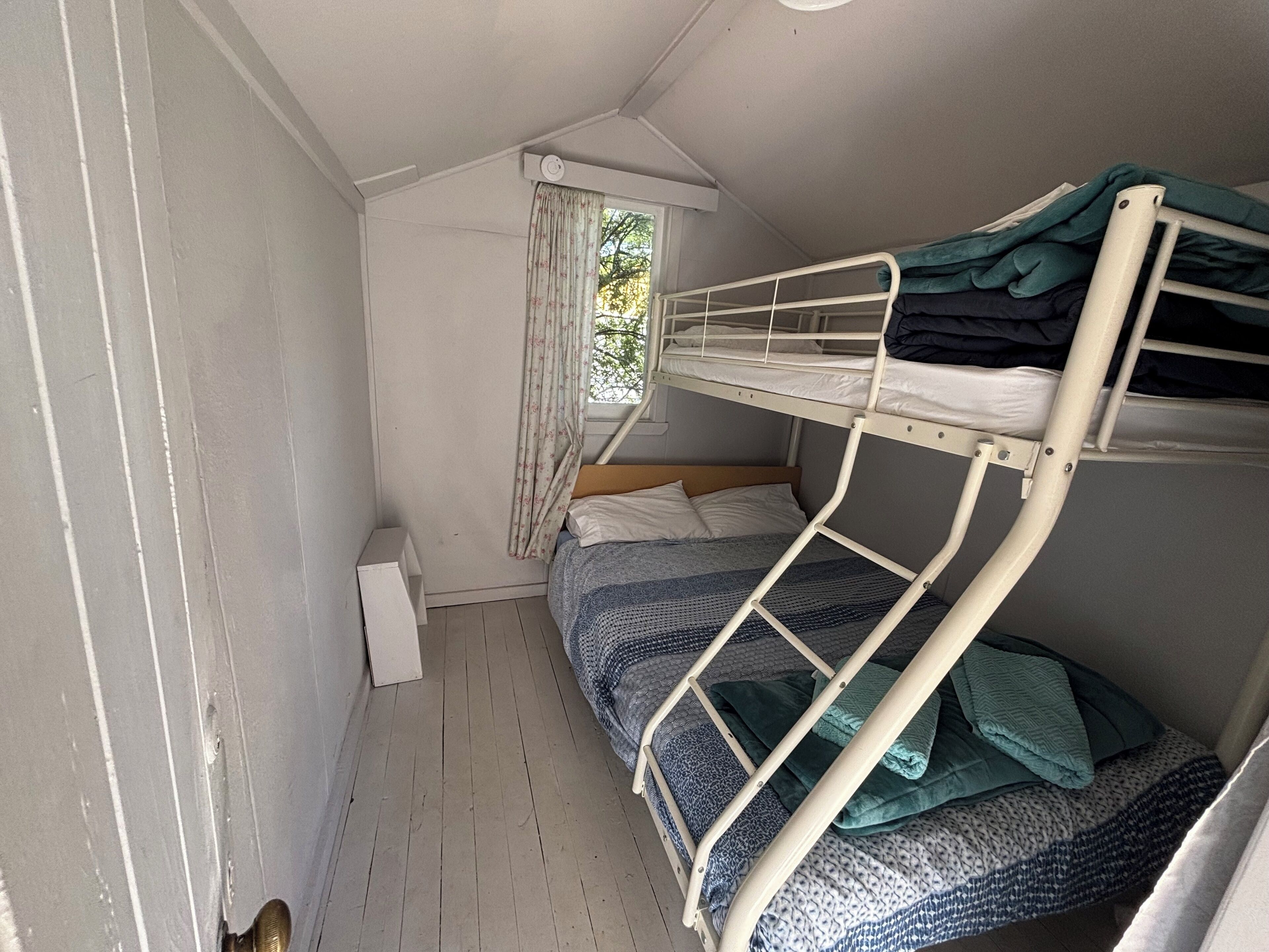 Une chambre avec un lit superposé, une fenêtre, une petite table blanche et une porte.
