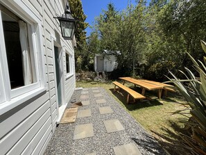 Une terrasse en bois avec une table de pique-nique et des bancs, entourée d’un chemin de gravier et de verdure.
