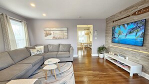 Una sala de estar moderna con un sofá seccional gris, una mesita blanca y un televisor de pantalla plana montado en una pared de madera.