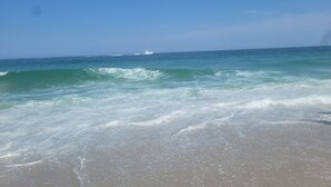 Una playa con olas y un yate a lo lejos.