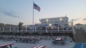 Un restaurante frente a la playa con terraza y un asta de bandera con la bandera estadounidense.