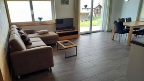 A living room with a sofa, TV, and a dining area with chairs and a table.