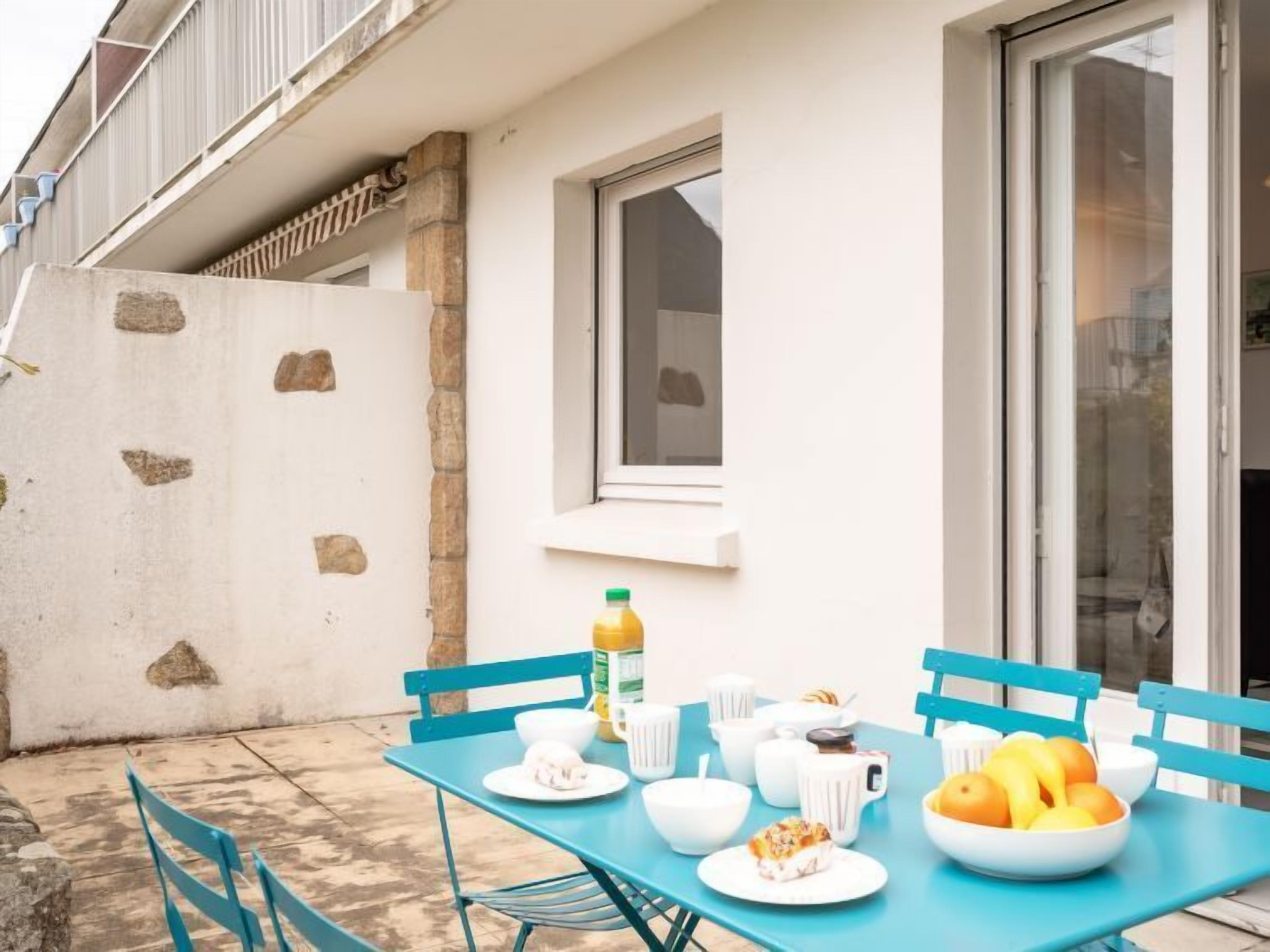 Une terrasse avec une table mise pour le petit-déjeuner, comprenant des bols, des tasses et un saladier rempli de fruits.