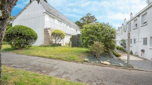 Une rue résidentielle bordée de maisons blanches, avec une chaussée pavée et un espace verdoyant agrémenté d’arbres et d’arbustes.